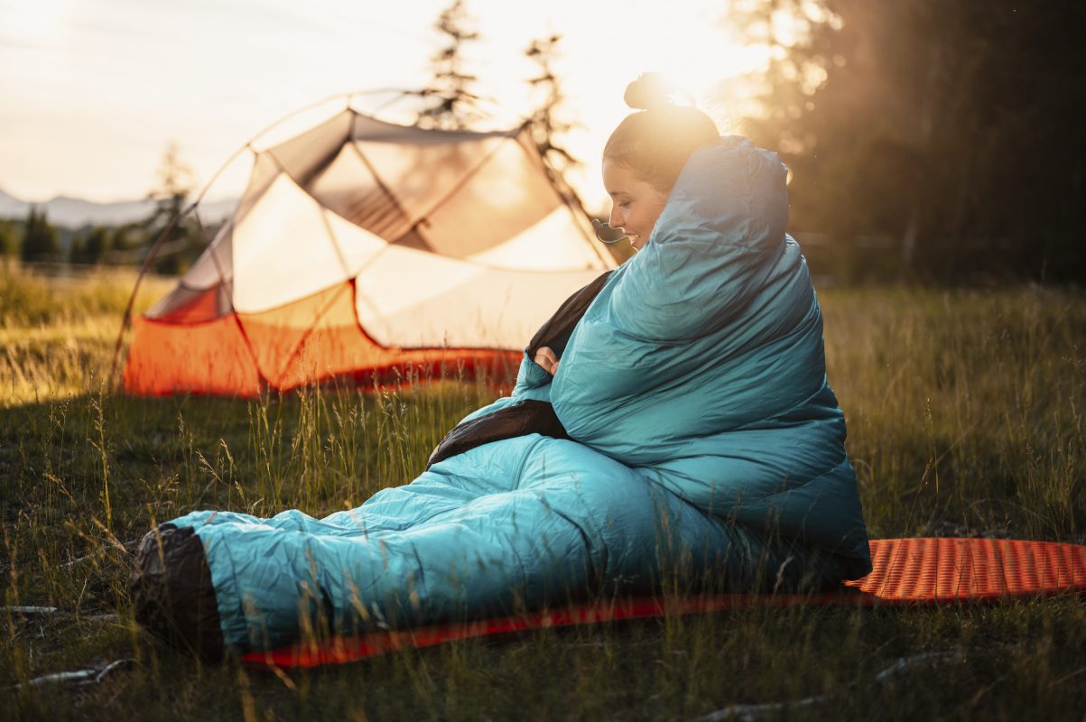 Woman relaxing and lie in a sleeping bag in the tent. Sunset camping in forest. Mountains landscape travel lifestyle camping. Summer travel outdoor adventure